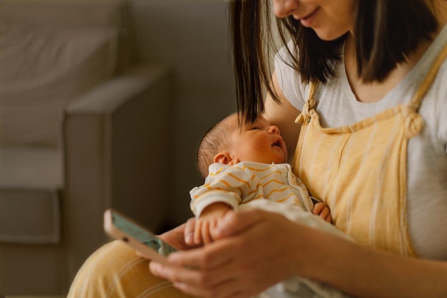 A mother with a newborn in her arms, using her mobile phone