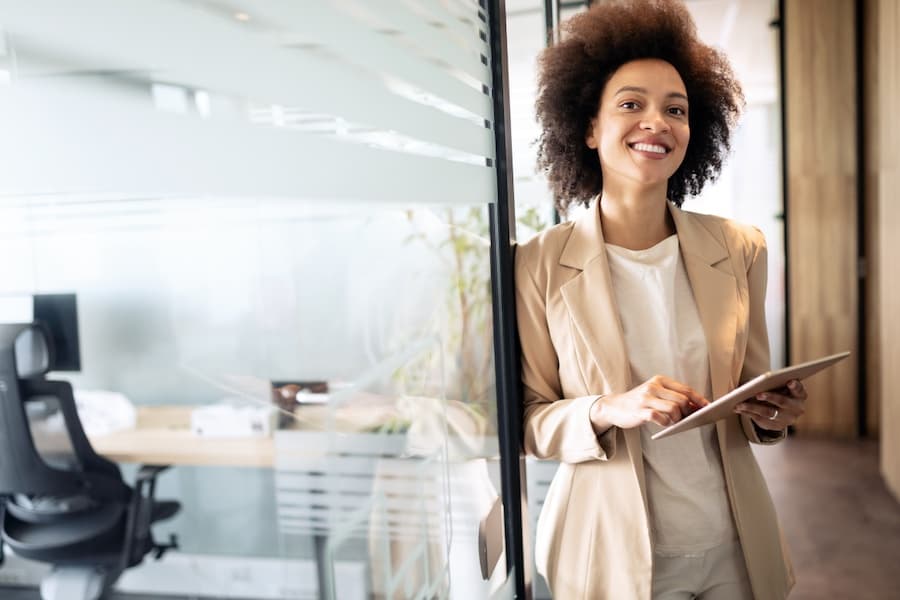 Woman in an office, smiling, holding a tablet, showing joy at work